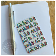 Load image into Gallery viewer, Colourful book-patterned book clip on a notebook with a pen